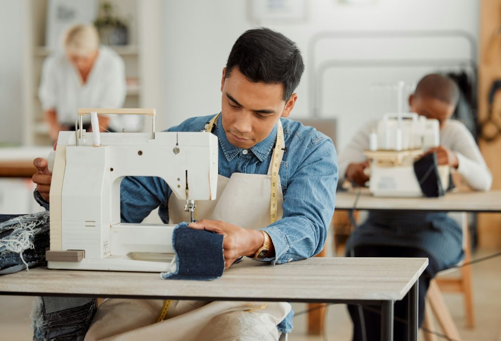 Creative fashion designer learning sewing skills on denim clothes in a clothing manufacturing facto