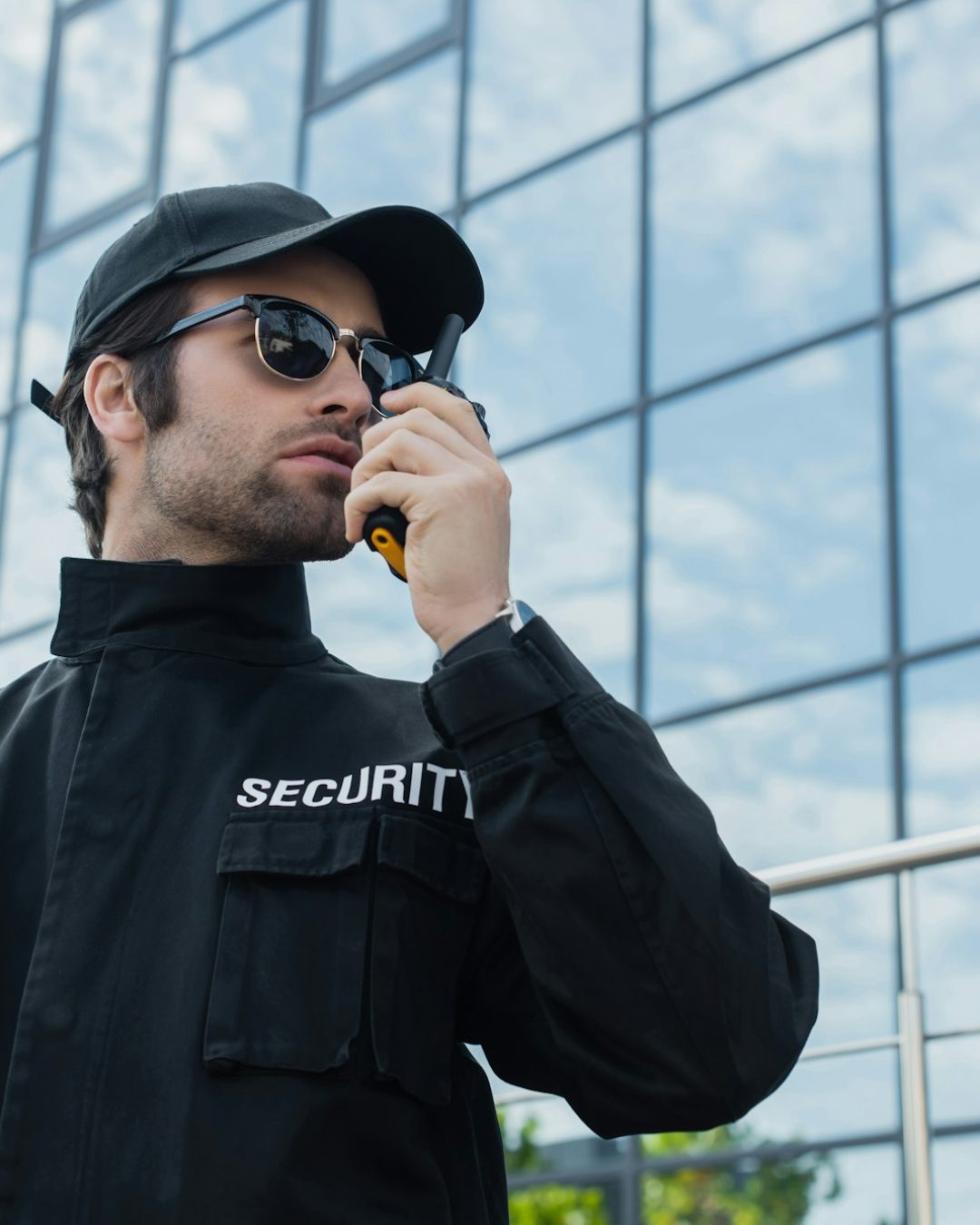 security man in sunglasses and black uniform talking on radio set outdoors